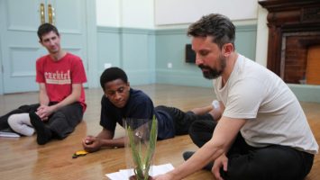 CDS Member Artist Hamish MacPherson holding a plant while sitting on the ground