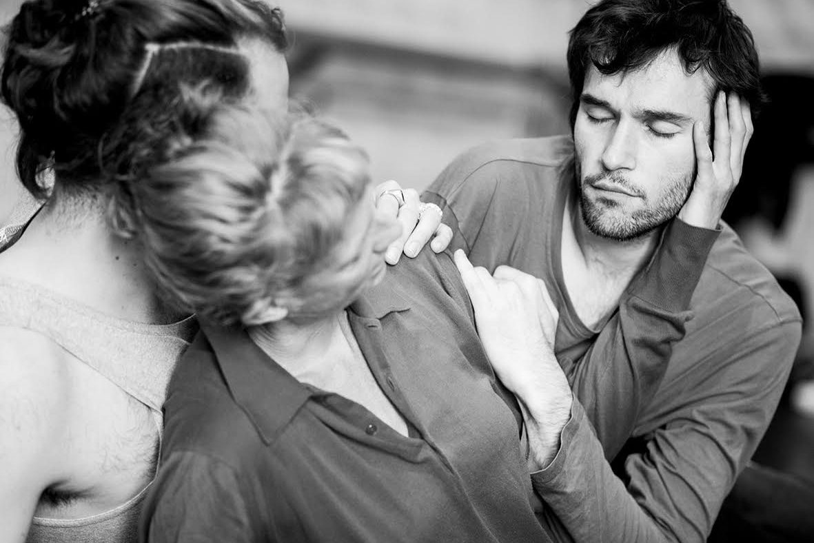 Three dancers lean in a close embrace