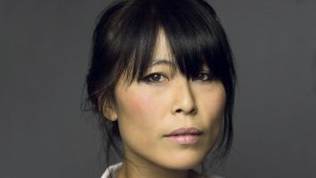 A photo of an East Asian woman. She has dark hair which is tied up, and a fringe which reaches her brown eyes