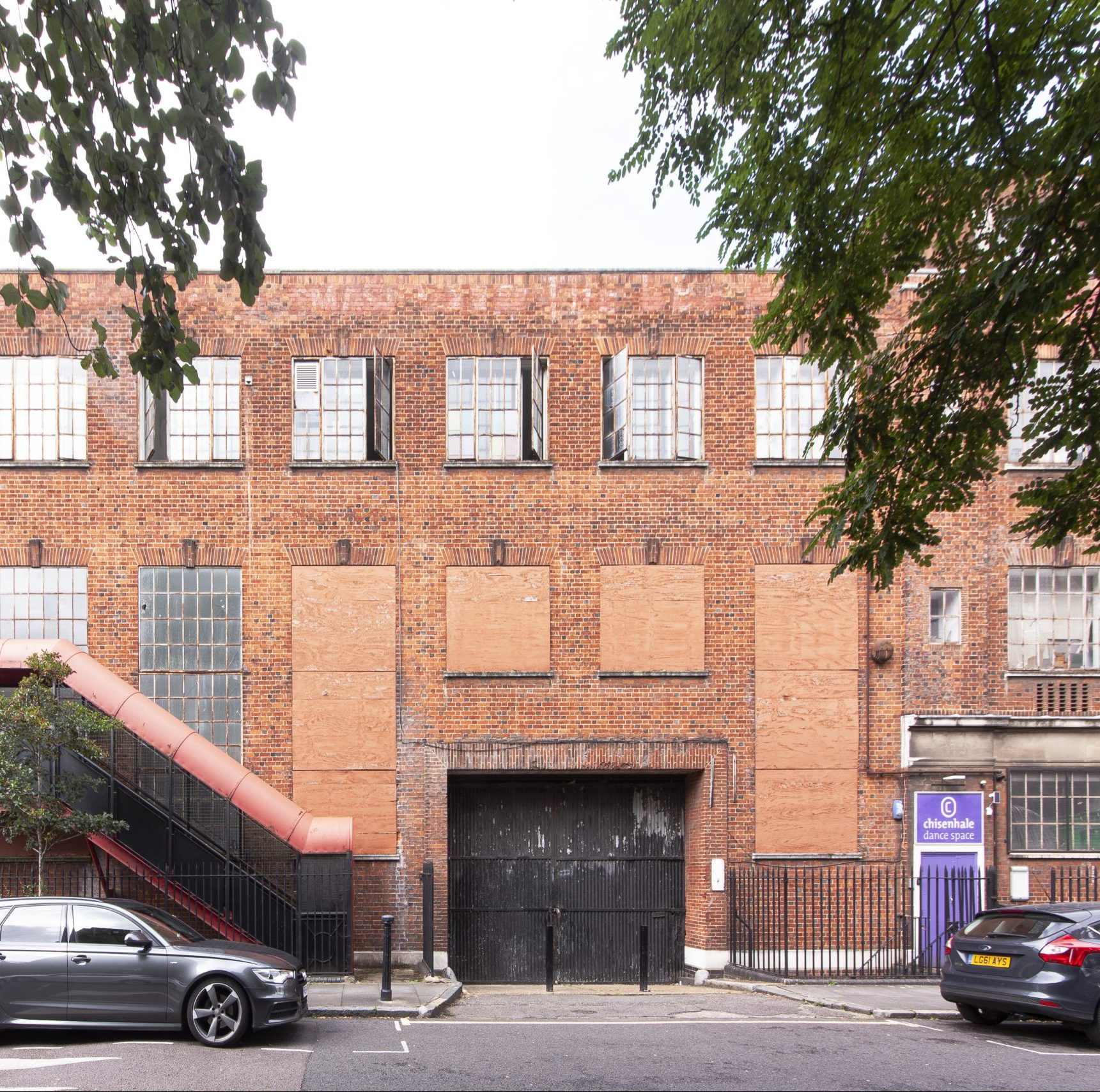 A red brick warehouse building with a red fire escape extending upwards to the left, and a bright purple door on the right